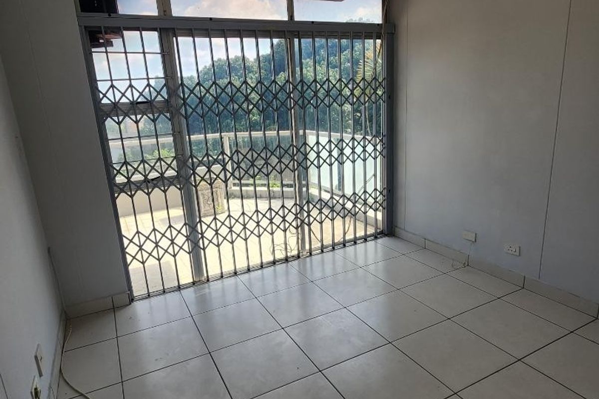 An empty living room featuring tiled flooring and a sliding glass door with a security gate, providing direct access to an outdoor balcony area.
