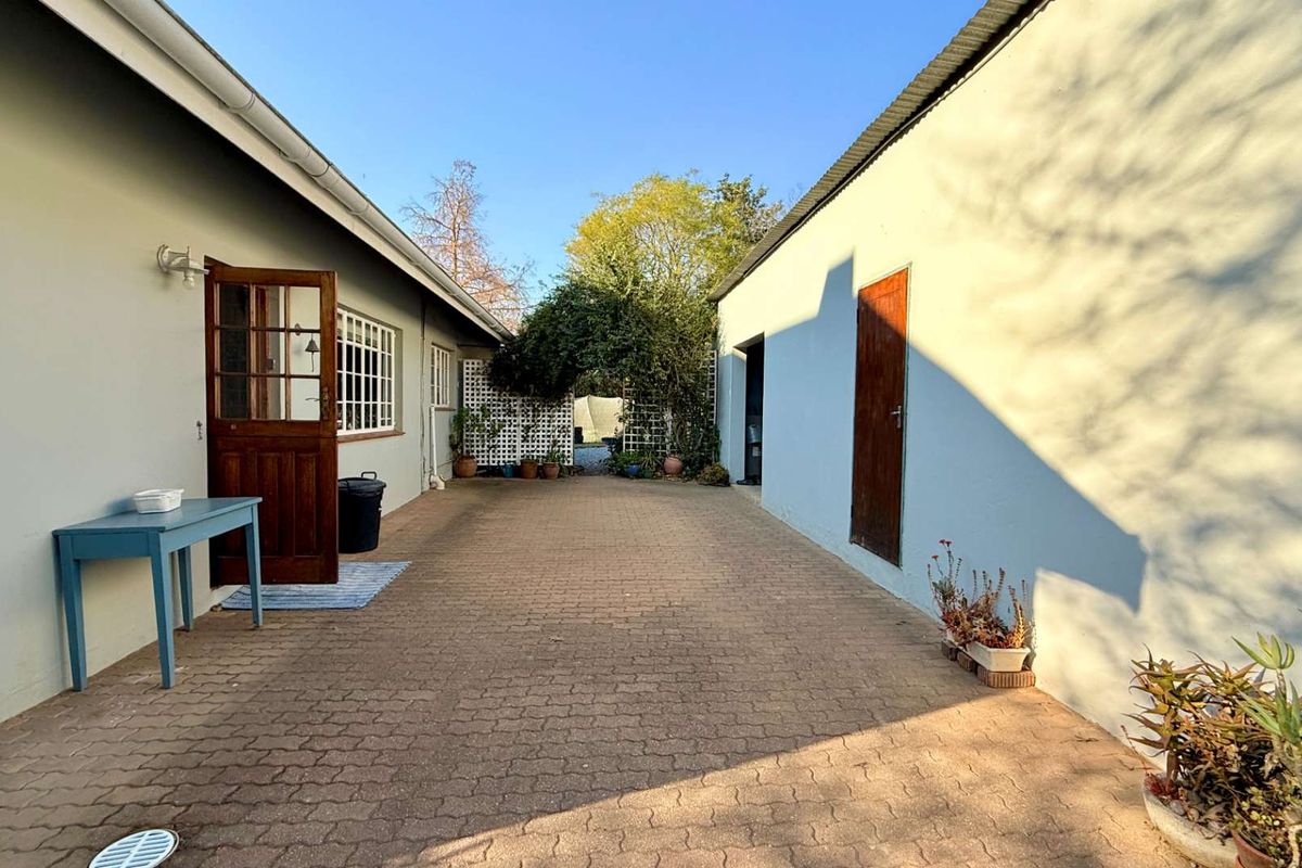 A paved outdoor courtyard area situated between two building structures, featuring a timber entrance door and lattice garden screening.
