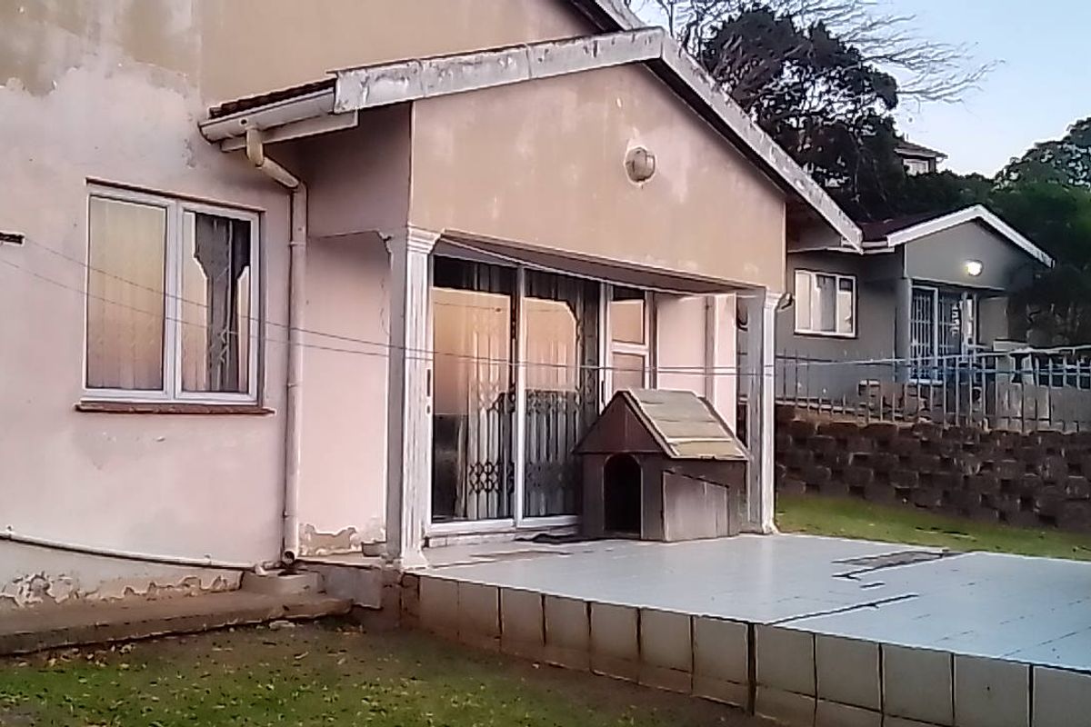 Rear exterior view of the townhouse featuring a tiled patio, sliding glass doors, and a retaining wall, showing signs of weathered exterior paint.