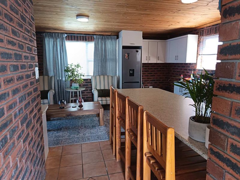Open-plan living and kitchen area featuring exposed brick walls, timber ceiling, tiled floors, and a central kitchen island with stone countertop.