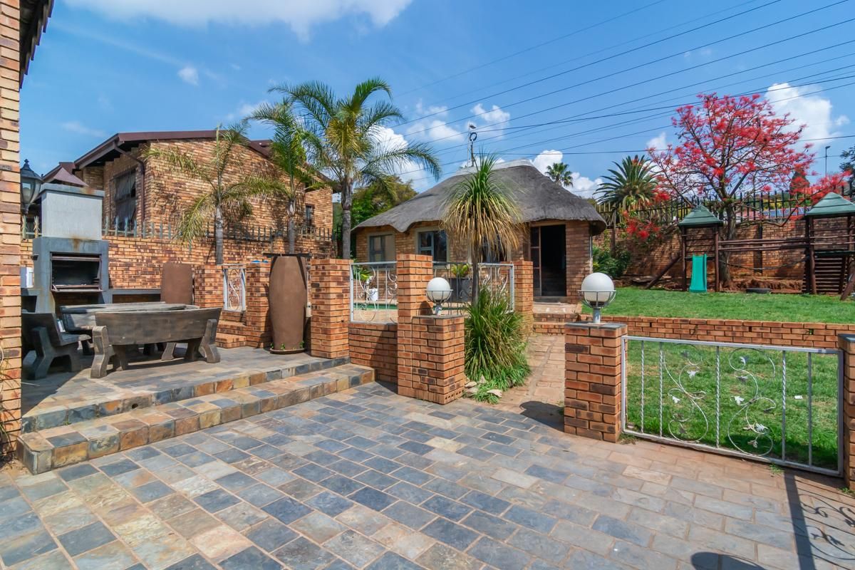 Rear garden area featuring a paved patio with a built-in braai, brick boundary walls, and a separate thatched-roof structure.