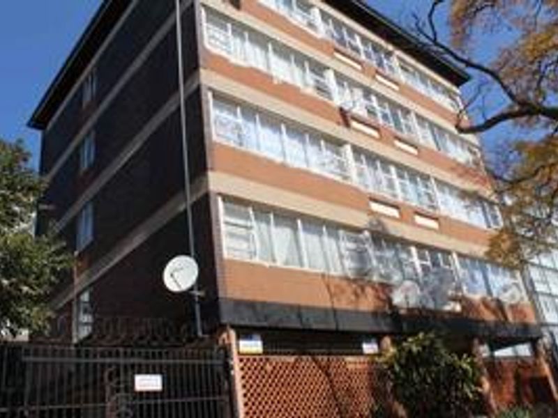 Exterior view of a multi-story apartment building featuring a brick facade, security fencing, and multiple satellite dish installations.