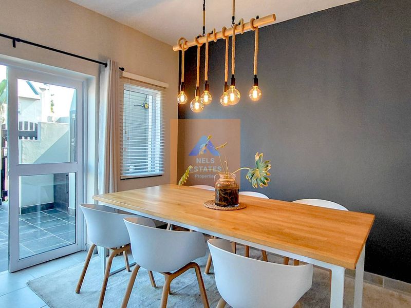A well-lit dining area featuring a modern accent wall, pendant lighting, and a sliding glass door providing access to the outdoor patio.
