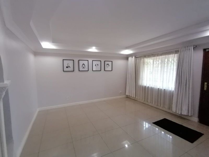 A bright and spacious living room featuring neutral tiled flooring, a modern recessed ceiling design, and large windows with security gates.