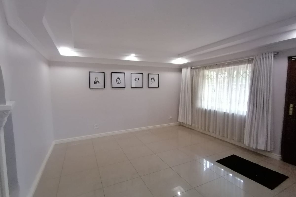 A bright and spacious living room featuring neutral tiled flooring, a modern recessed ceiling design, and large windows with security gates.