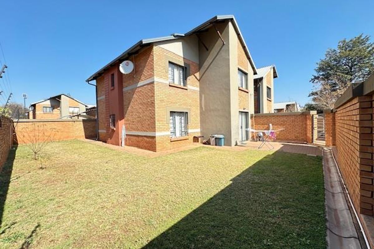Rear view of the townhouse featuring a private garden, brick exterior walls, and a paved patio area.