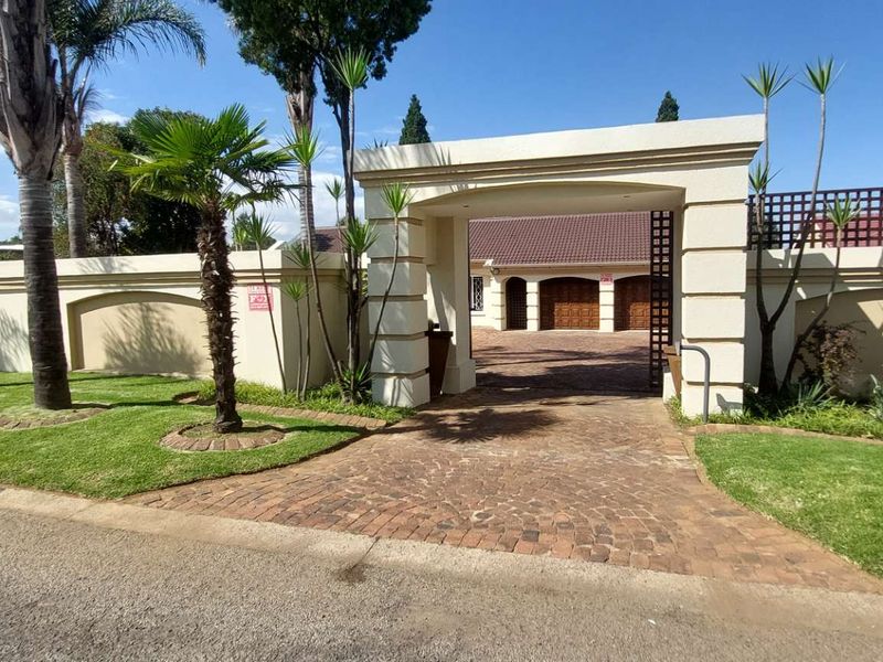 Front view of the property featuring a paved driveway, secure boundary wall, gated entrance, and well-maintained garden leading to the garage area.