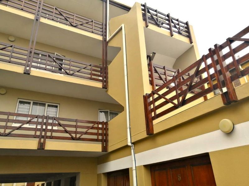 Exterior view of a multi-level apartment building featuring timber balcony railings and a ground-level entrance.