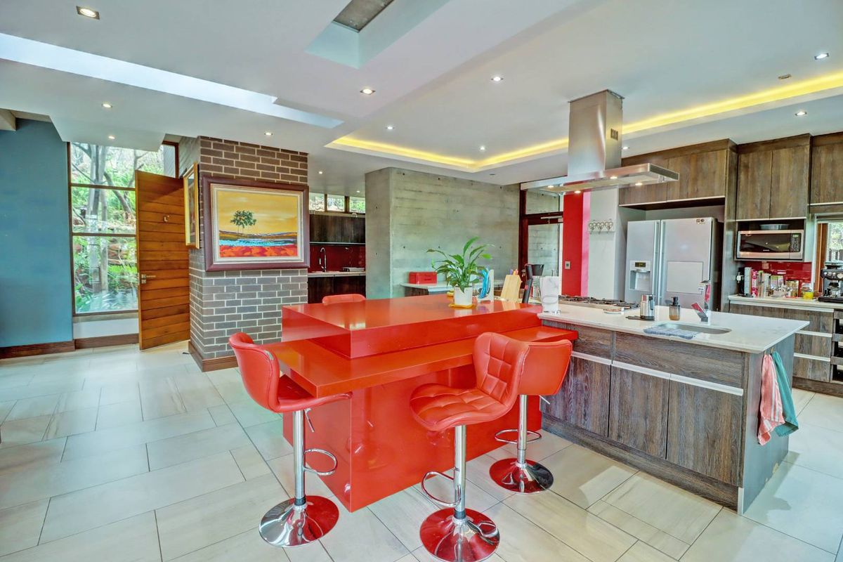Modern kitchen featuring a large red island, stone countertops, stainless steel extractor fan, and a mix of exposed brick and concrete architectural elements.