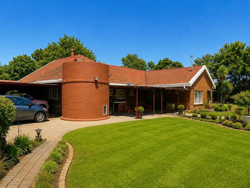 A well-maintained brick house featuring a covered patio, paved driveway, and a spacious, landscaped garden with mature greenery.