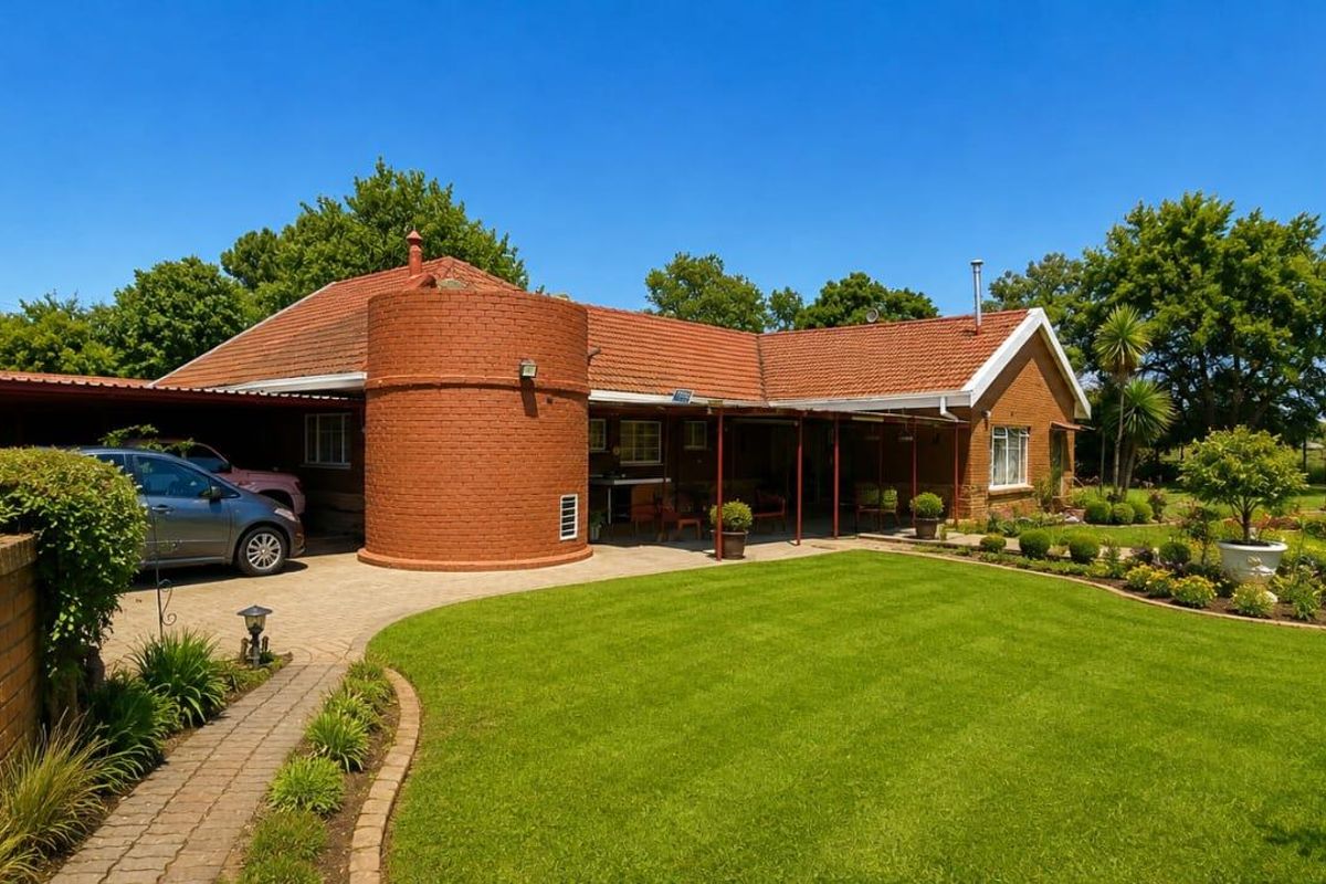 A well-maintained brick house featuring a covered patio, paved driveway, and a spacious, landscaped garden with mature greenery.
