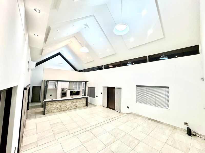 Spacious open-plan living area featuring a vaulted ceiling, modern tiled floors, clerestory windows, and a contemporary kitchen with a stone-clad breakfast bar.
