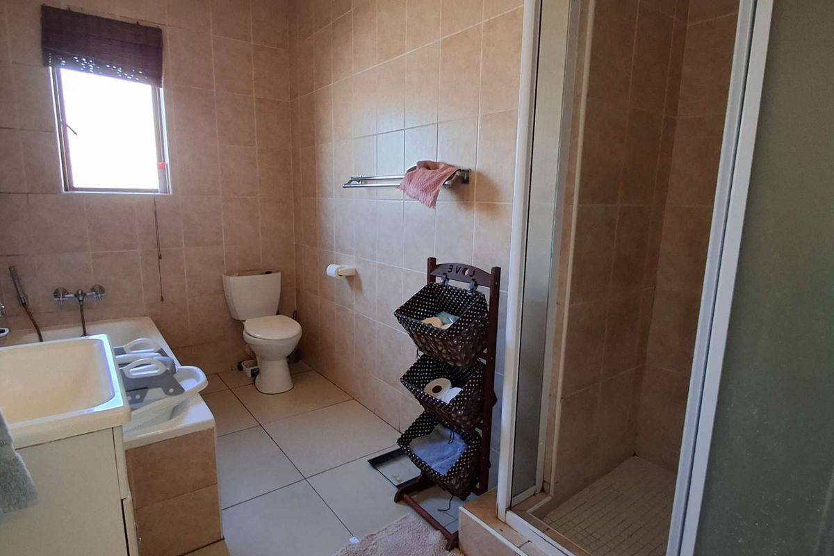 A functional bathroom featuring a bathtub, separate shower enclosure, toilet, and vanity basin with neutral wall and floor tiling.