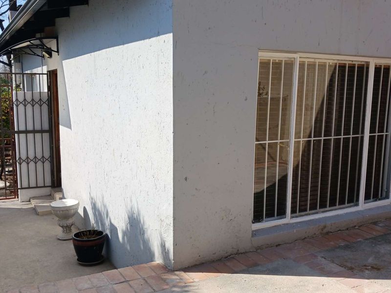 Rear exterior view of the cottage featuring a concrete patio, brick paving, and security bars on the windows.