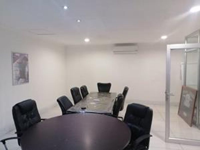 A functional office space featuring tiled flooring, recessed downlighting, and a wall-mounted air conditioning unit, accessible via an aluminium framed glass door.