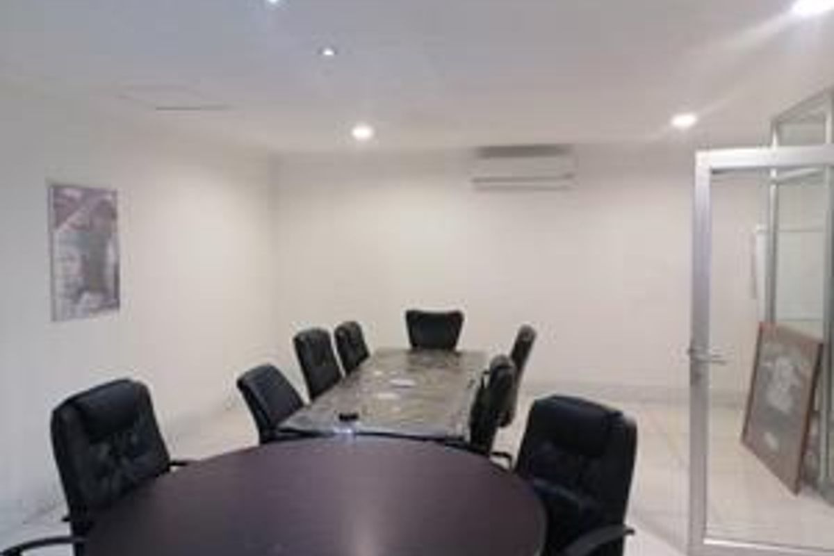 A functional office space featuring tiled flooring, recessed downlighting, and a wall-mounted air conditioning unit, accessible via an aluminium framed glass door.