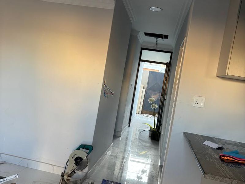 A hallway under construction featuring polished porcelain floor tiles, recessed lighting, and a stone countertop, showing ongoing renovation work.