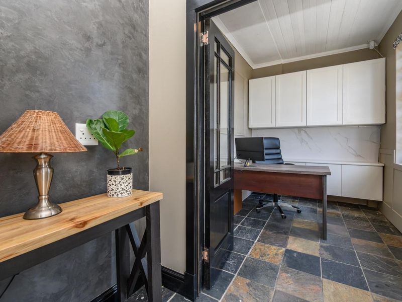 A well-appointed home office featuring built-in cabinetry, stone-look splashback, slate tile flooring, and a classic french door entrance.