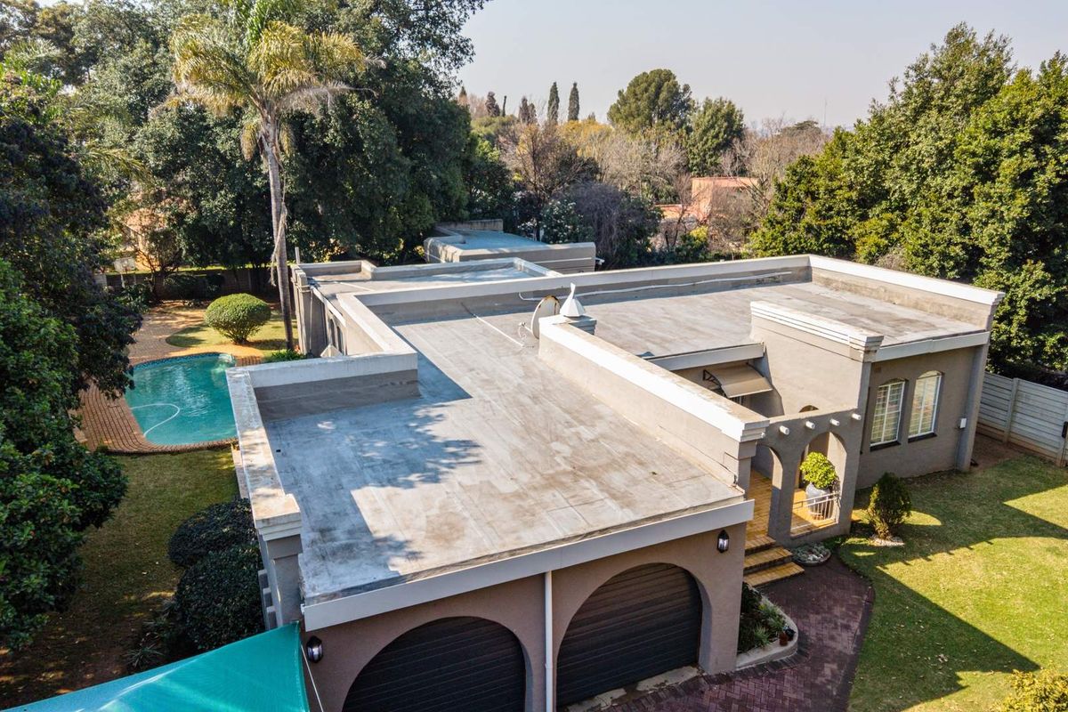 Aerial view of a residential property featuring a flat roof, double garage, arched entrance, and a swimming pool set within a landscaped garden.