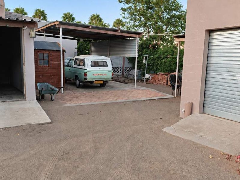 Rear exterior area featuring a carport, paved driveway section, and access to a garage with a roller shutter door.