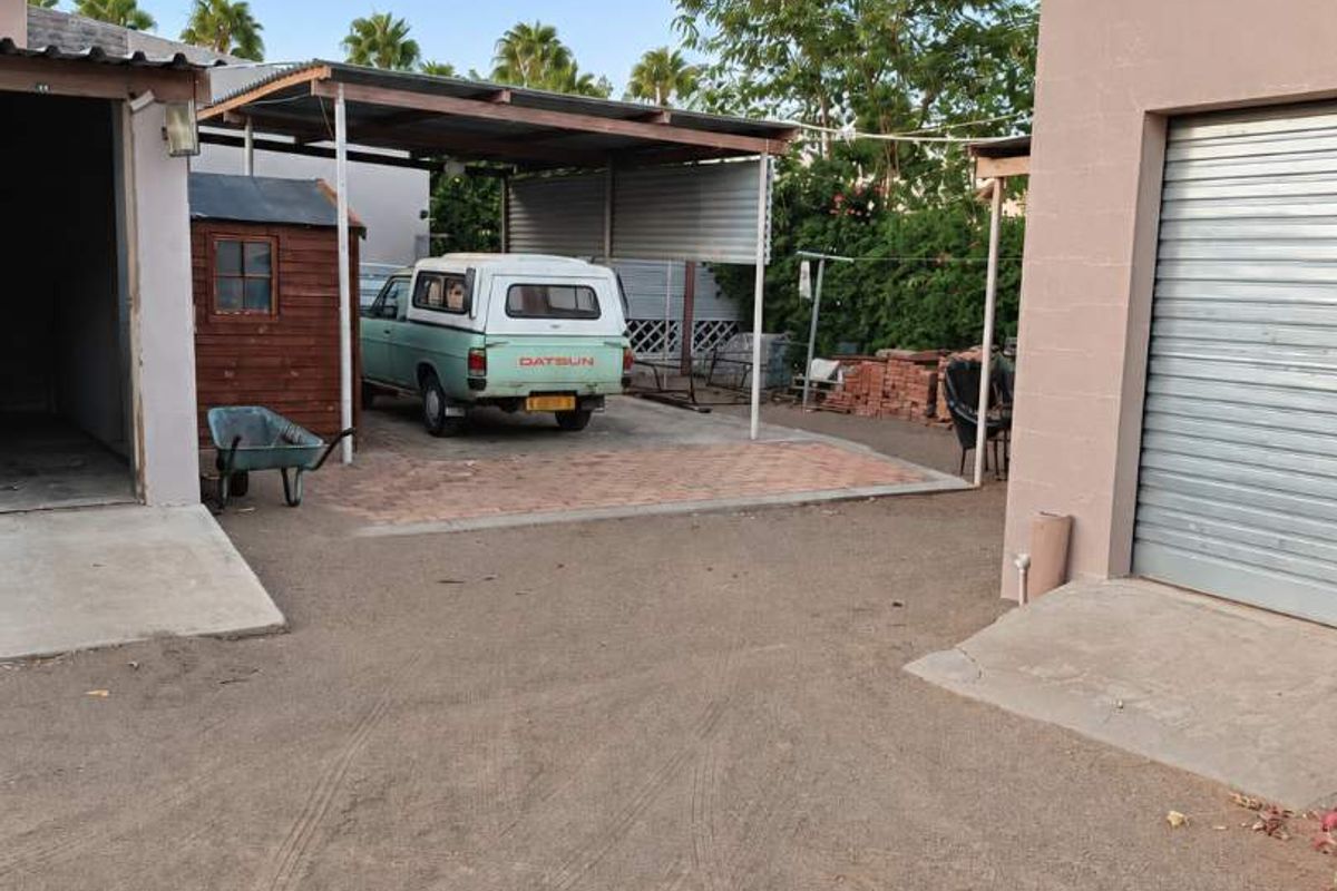Rear exterior area featuring a carport, paved driveway section, and access to a garage with a roller shutter door.