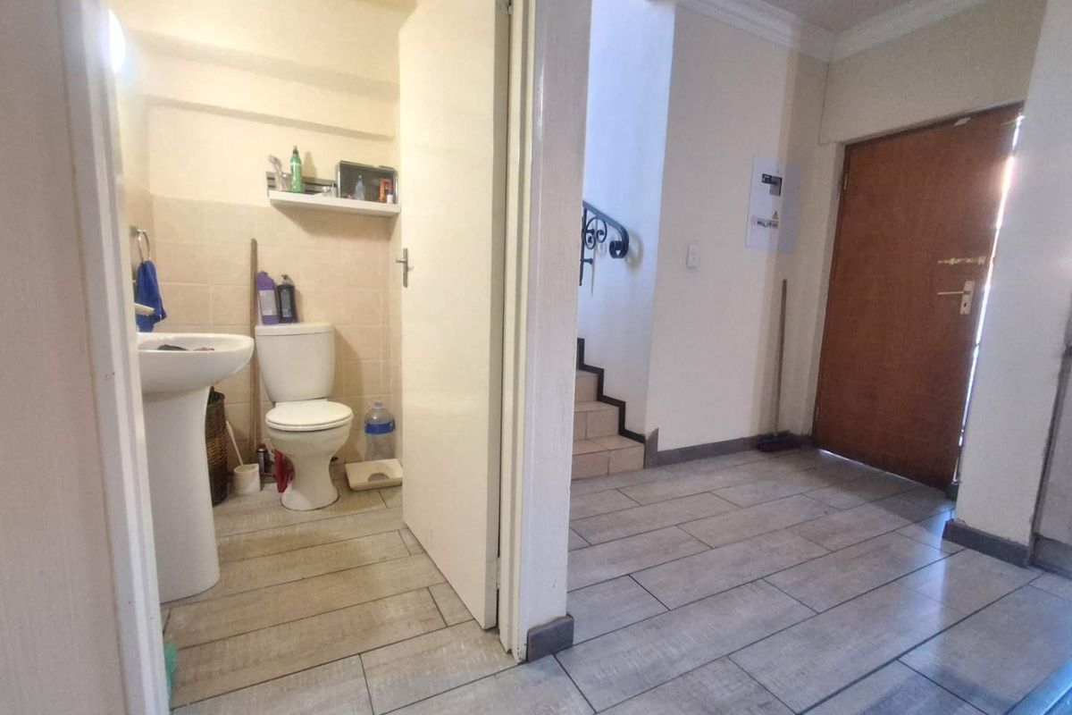 A functional ground floor bathroom featuring a pedestal basin and toilet, adjacent to the main entrance and staircase area.