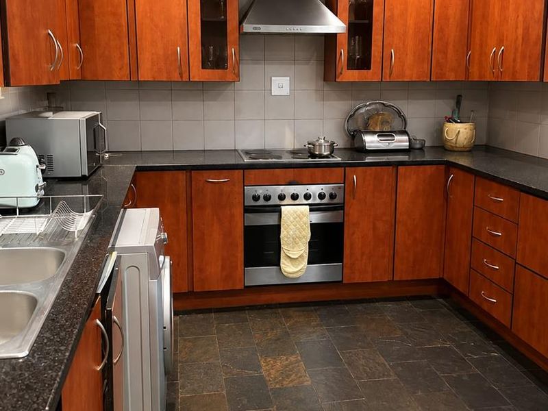 A functional kitchen featuring cherry wood cabinetry, granite countertops, slate flooring, and integrated stainless steel appliances including an oven and extractor fan.