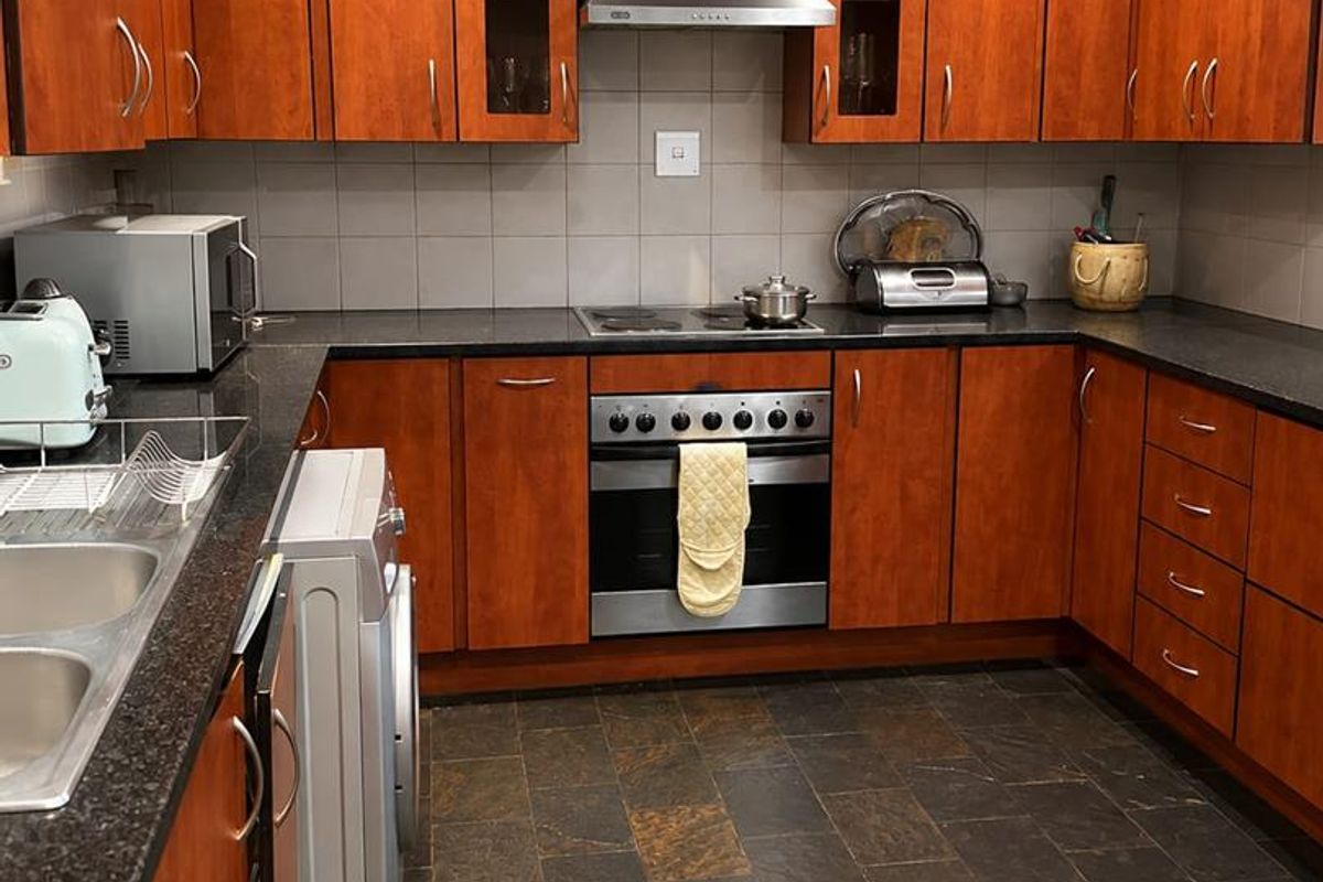 A functional kitchen featuring cherry wood cabinetry, granite countertops, slate flooring, and integrated stainless steel appliances including an oven and extractor fan.