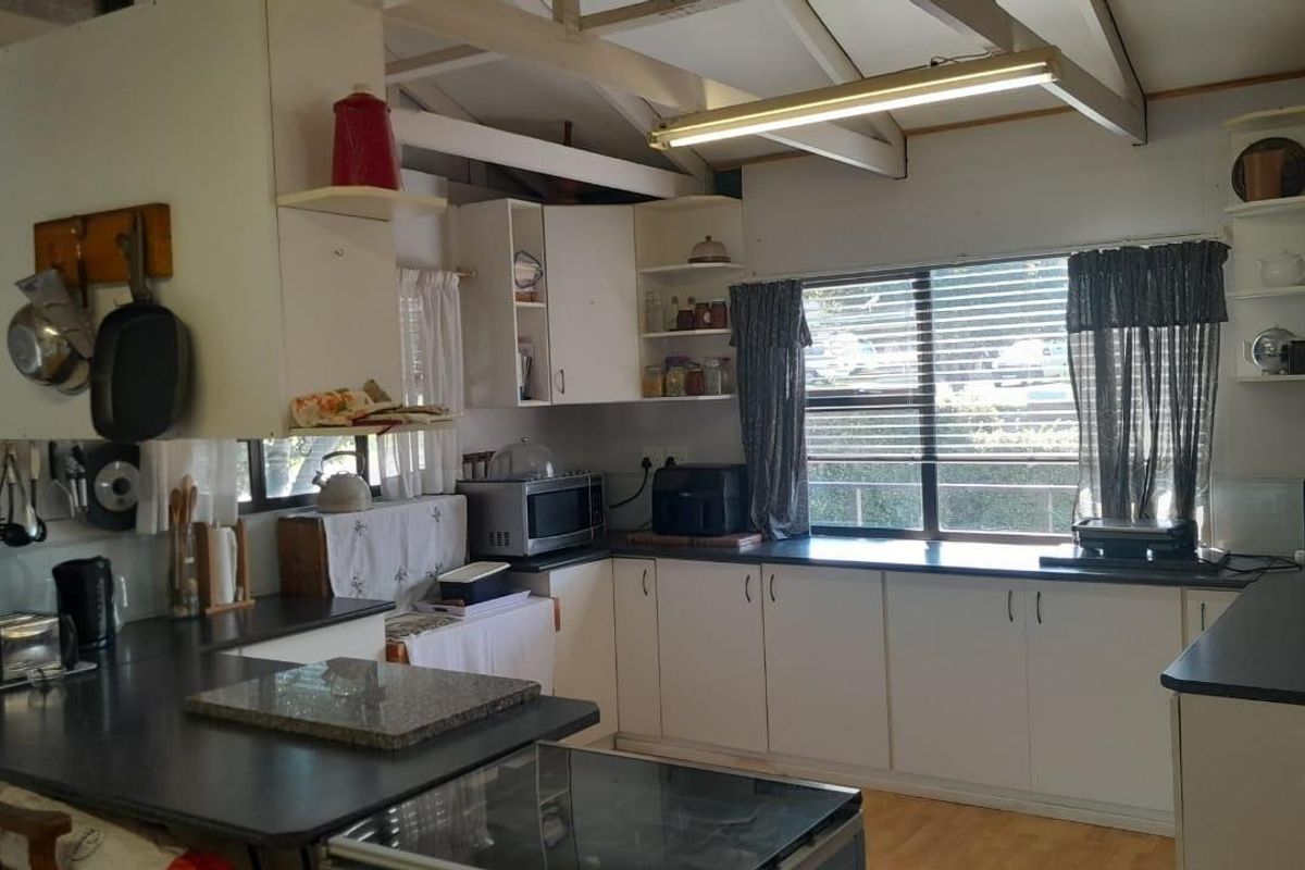 A functional kitchen featuring white cabinetry, dark countertops, and exposed timber ceiling beams, offering a practical layout with ample natural light.