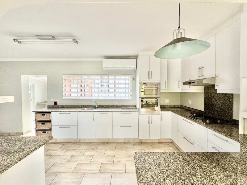 A modern kitchen featuring white cabinetry, granite countertops, built-in appliances including an oven and hob, and tiled flooring.