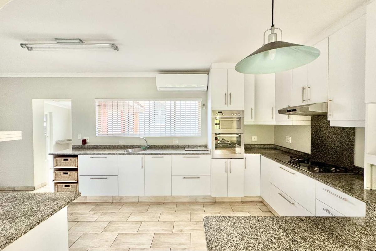 A modern kitchen featuring white cabinetry, granite countertops, built-in appliances including an oven and hob, and tiled flooring.