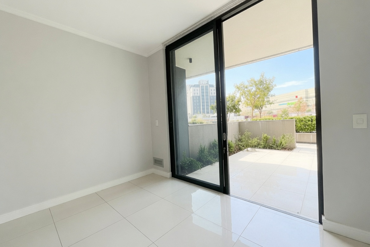 A bright, empty living area featuring large sliding glass doors that open onto a private tiled balcony with urban views.
