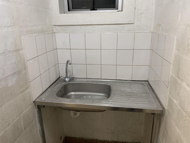 A functional utility space featuring a stainless steel sink with a tiled splashback and a small window, suitable for laundry or prep tasks.