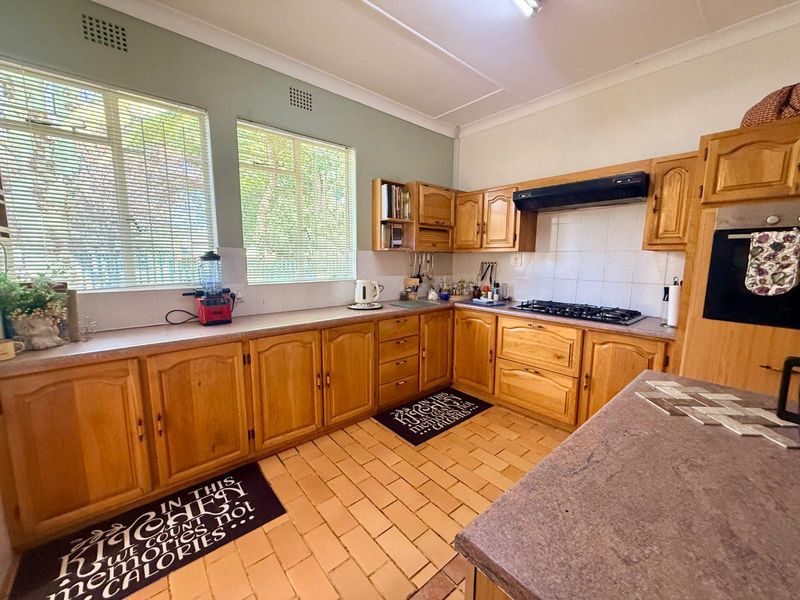 A functional kitchen featuring traditional wooden cabinetry, laminate countertops, a gas hob, built-in oven, and tiled flooring with ample natural light.