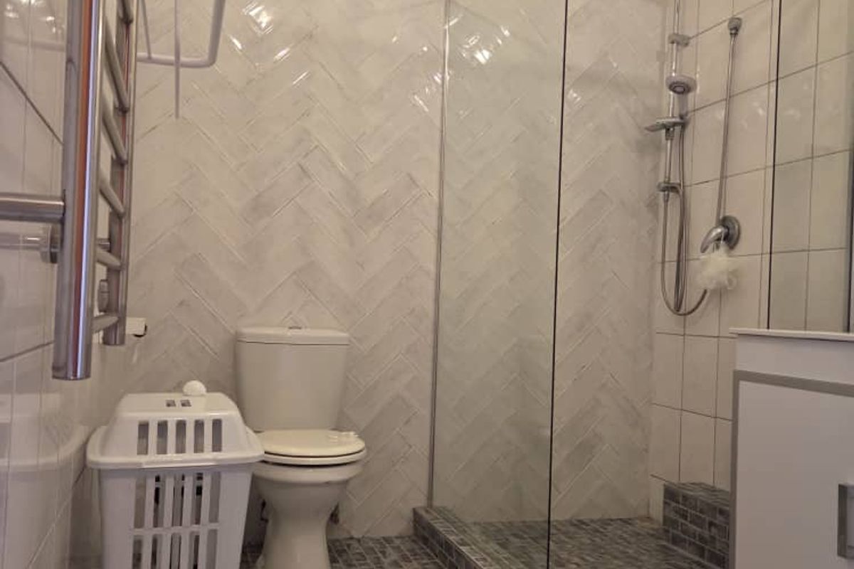 Modern bathroom featuring a glass-enclosed walk-in shower, herringbone wall tiling, a vanity unit, and a heated towel rail.