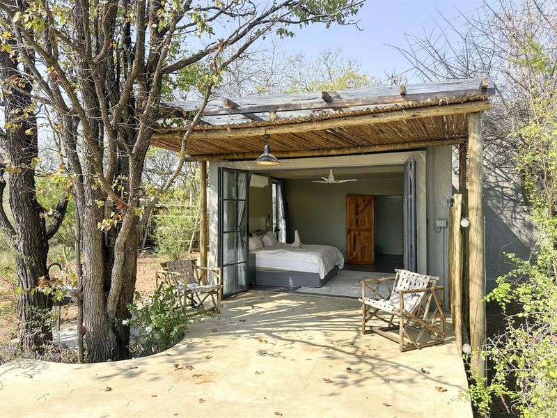A covered outdoor patio area featuring a thatched roof, timber support posts, and bi-fold glass doors leading into a bedroom suite.