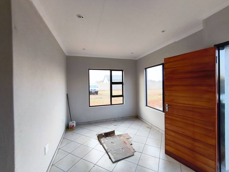 A bright, empty bedroom featuring neutral wall finishes, tiled flooring, recessed ceiling lighting, and modern aluminium-framed windows.