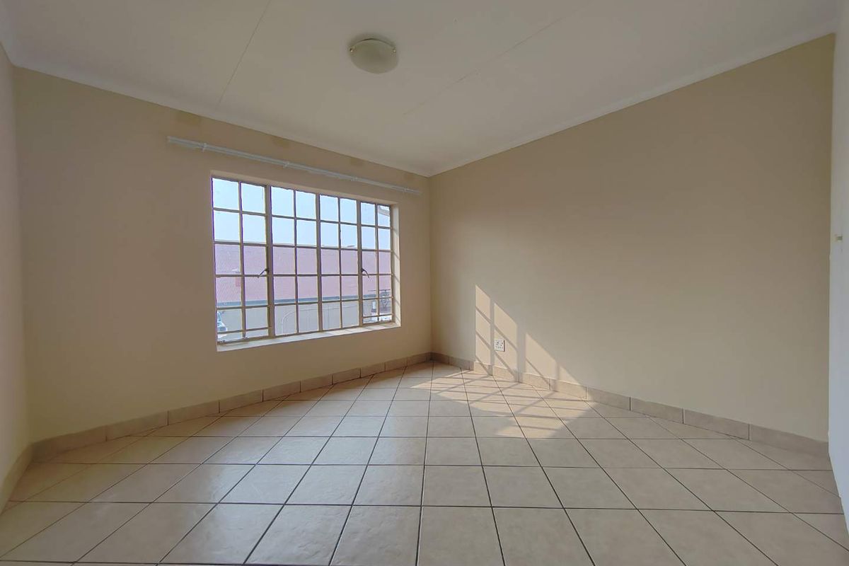 A bright, empty bedroom featuring neutral wall paint, tiled flooring, and a large grid-pattern window allowing for natural light.