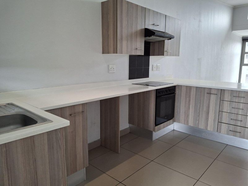 Modern kitchen featuring wood-look cabinetry, white countertops, integrated electric oven and hob, and neutral floor tiling.