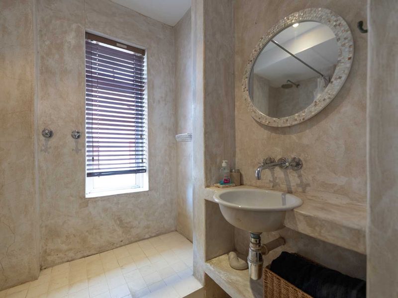 A rustic-style bathroom featuring a built-in concrete vanity, wall-mounted basin, and a tiled shower area with a neutral textured wall finish.