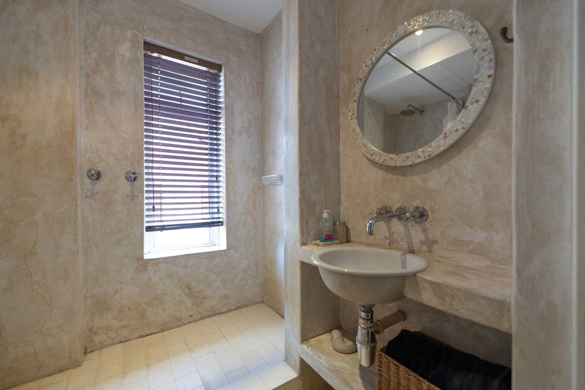 A rustic-style bathroom featuring a built-in concrete vanity, wall-mounted basin, and a tiled shower area with a neutral textured wall finish.