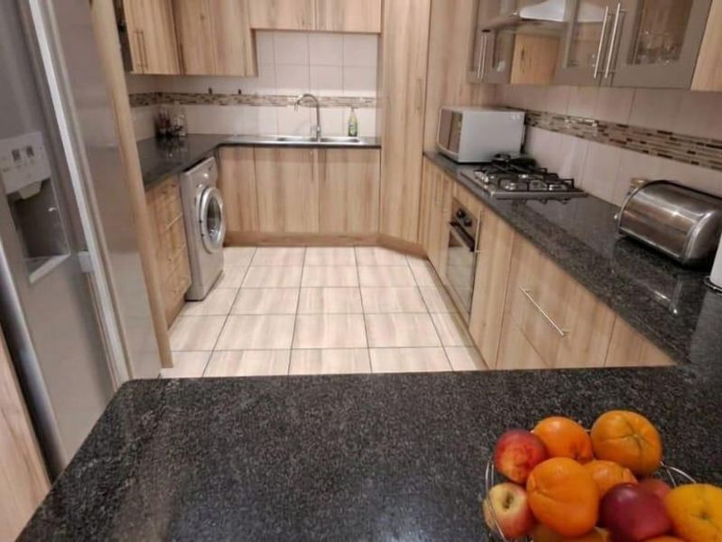 A well-maintained kitchen featuring modern wood-finish cabinetry, granite countertops, a gas hob, built-in oven, and tiled flooring.