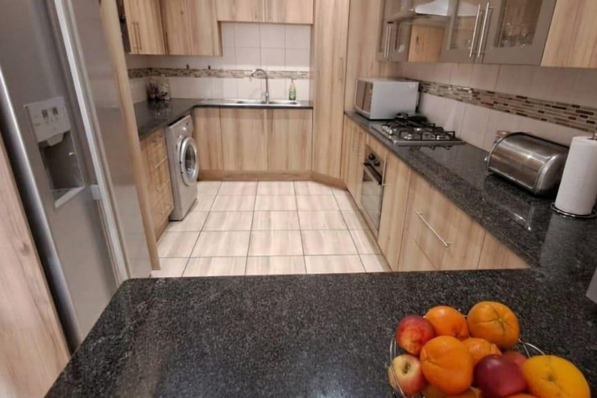 A well-maintained kitchen featuring modern wood-finish cabinetry, granite countertops, a gas hob, built-in oven, and tiled flooring.