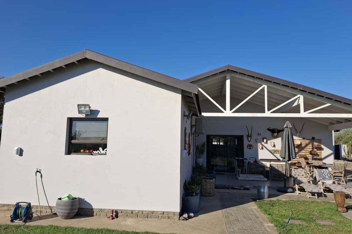Rear view of the property featuring a covered patio area with exposed roof trusses, paved walkway, and well-maintained exterior walls.