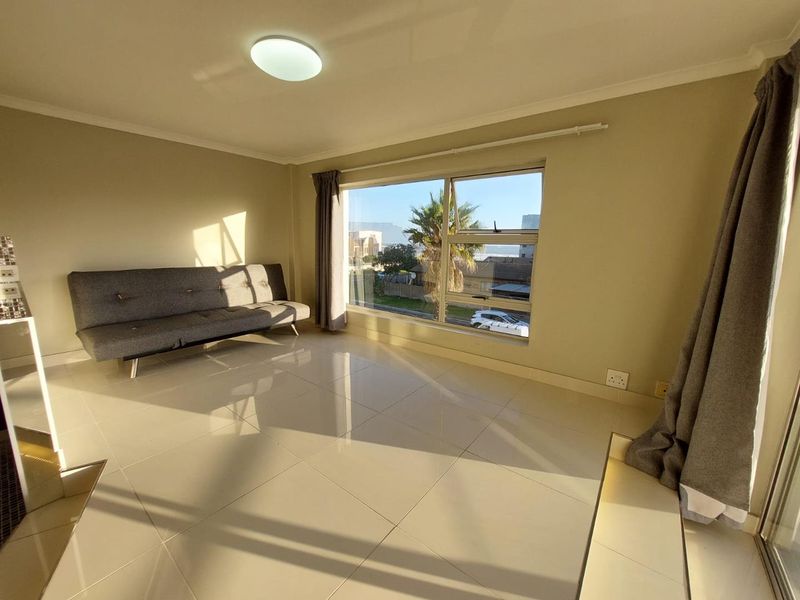 A bright and spacious living area featuring large windows, neutral tiled flooring, and clean finishes, offering a comfortable and well-lit living space.
