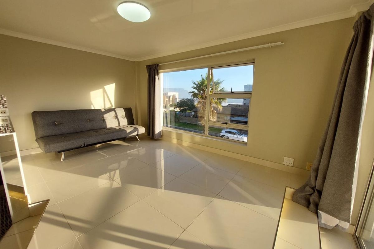 A bright and spacious living area featuring large windows, neutral tiled flooring, and clean finishes, offering a comfortable and well-lit living space.