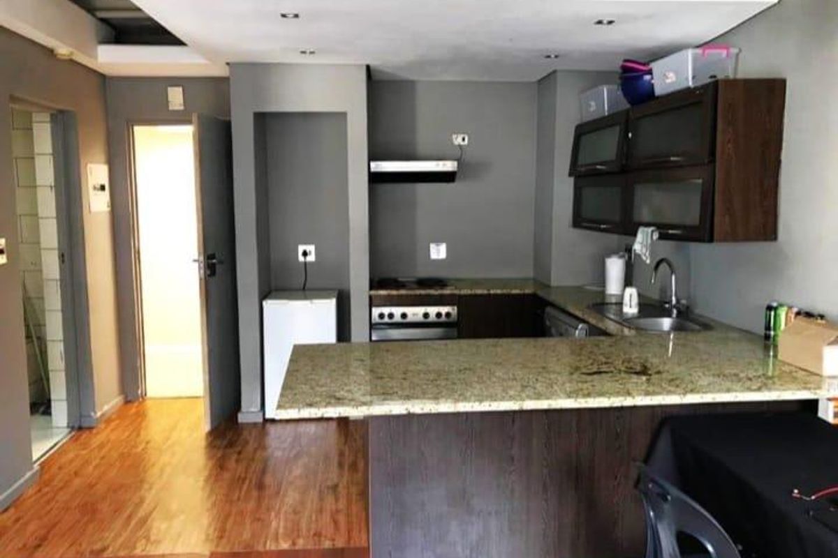 Compact kitchen featuring granite countertops, dark wood cabinetry, built-in stove with extractor fan, and a breakfast bar, opening into the main living area.
