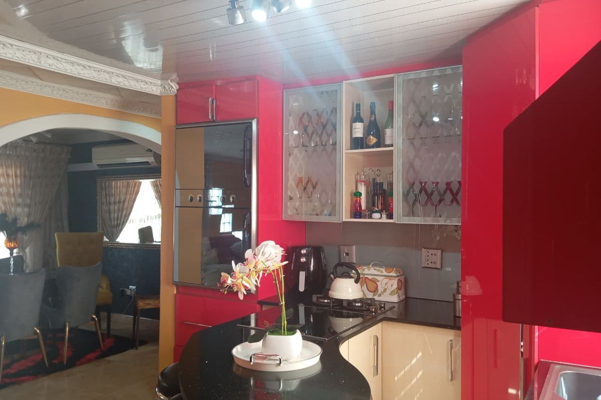 A kitchen featuring high-gloss red cabinetry, stone countertops, a breakfast bar, and built-in appliances, with an open-plan layout leading to the dining area.