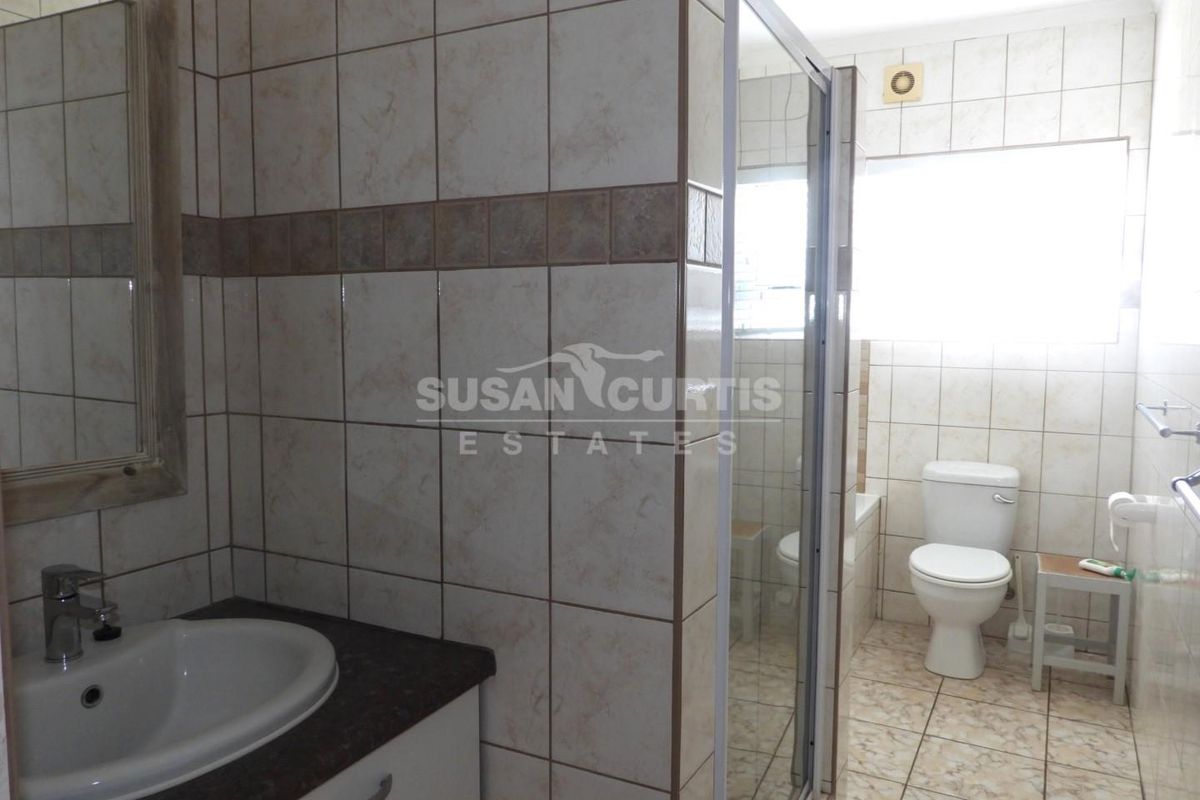 A functional bathroom featuring a vanity with a drop-in basin, a separate shower enclosure, and a toilet, finished with neutral wall and floor tiles.
