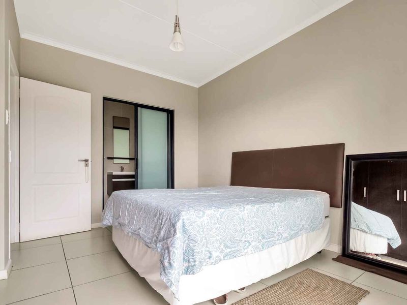 A well-maintained bedroom featuring neutral wall tones, tiled flooring, and direct access to an en-suite bathroom.